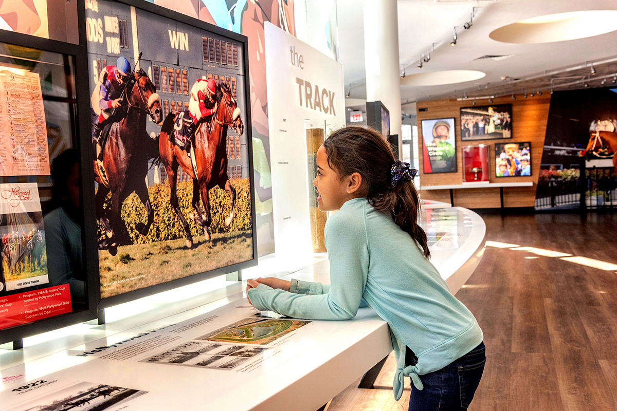 A kid using an interactive exhibit at the national thoroughbred racing museum and hall of fame